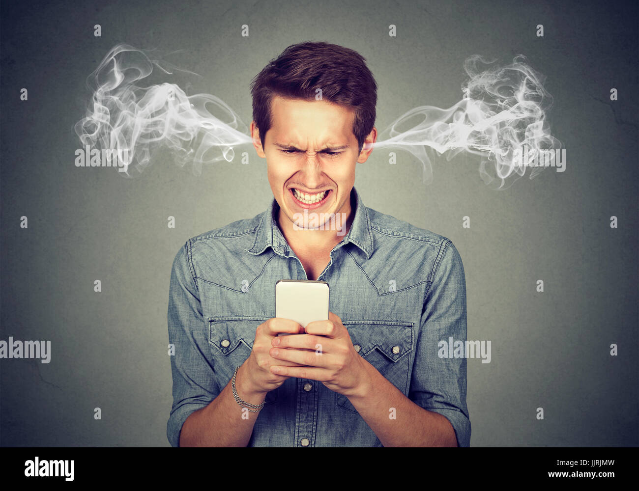 Frustrated angry man reading a text message on his smartphone blowing steam coming out of ears Stock Photo