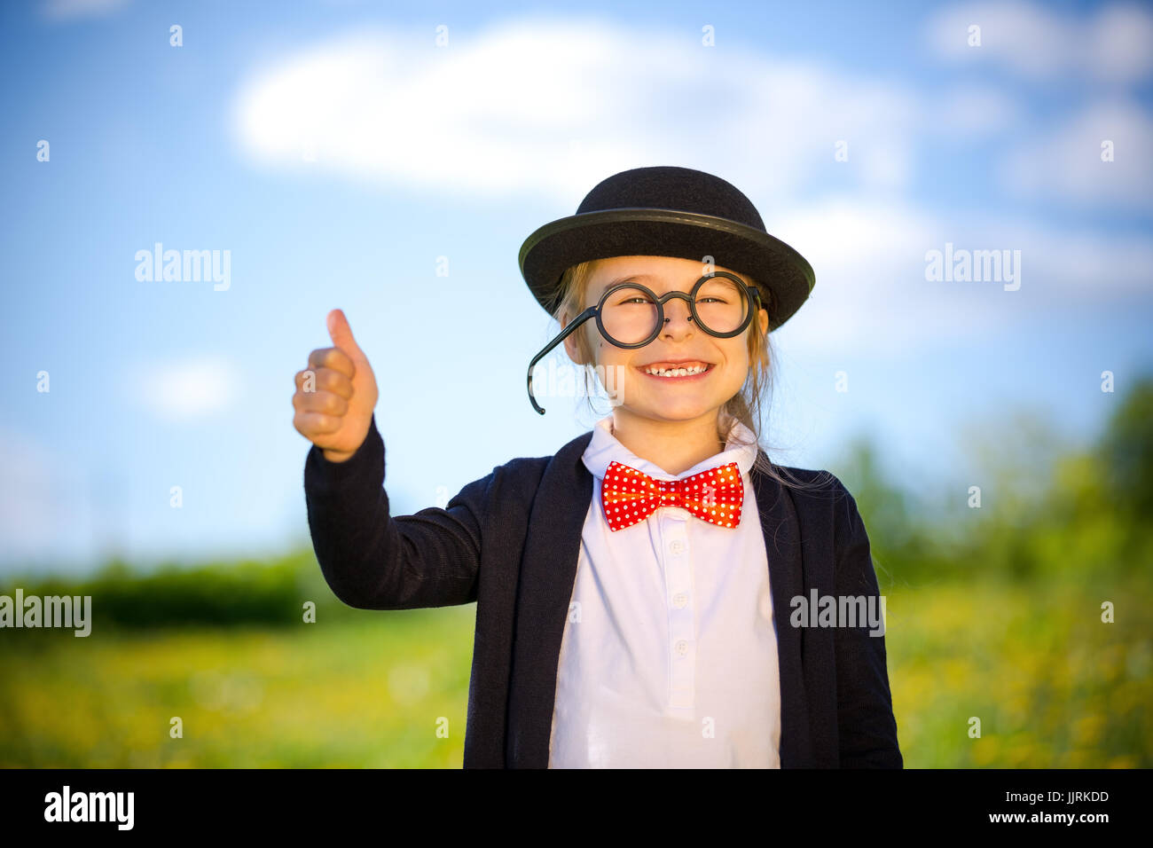 Funny little girl in bow tie and bowler hat showing thumb up. Stock Photo