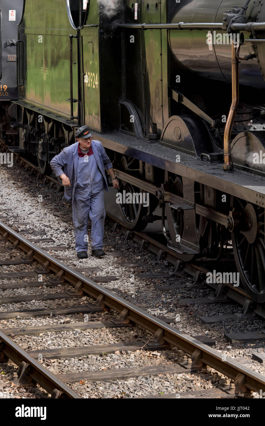 Train driver walks on tracks by steam locomotive, BR (Midland Railway) 4F 0-6-0 43924, at station - Keighley and Worth Valley Railway, England, UK. Stock Photo