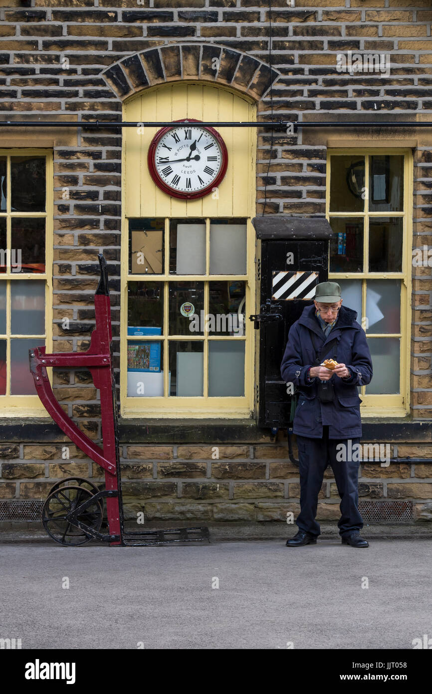 Man next to old booking office, clock & luggage trolley on platform - historic Oxenhope Station, Keighley & Worth Valley Railway station, England, UK. Stock Photo