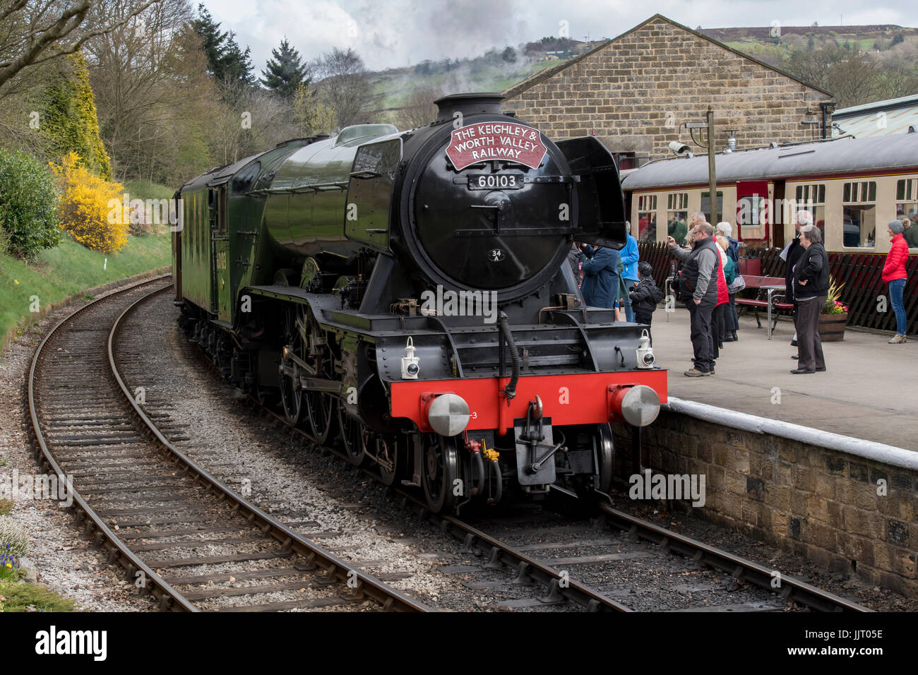 People on platform & iconic steam locomotive 60103 Flying Scotsman on tracks puffing smoke - Keighley and Worth Valley Railway station, England, UK. Stock Photo