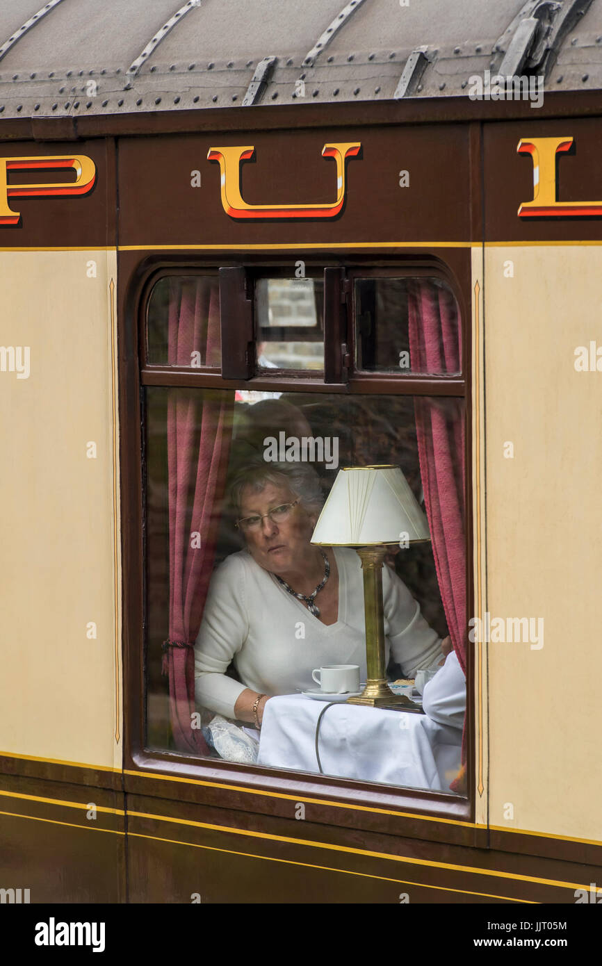 Lady in Pullman coach having afternoon tea looks out of iconic steam locomotive, 60103 Flying Scotsman - Keighley & Worth Valley Railway, England, UK. Stock Photo