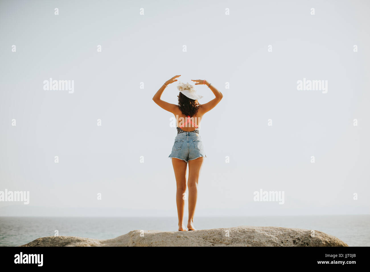 Pretty young woman at sea on the stony shore on a sunny day Stock Photo
