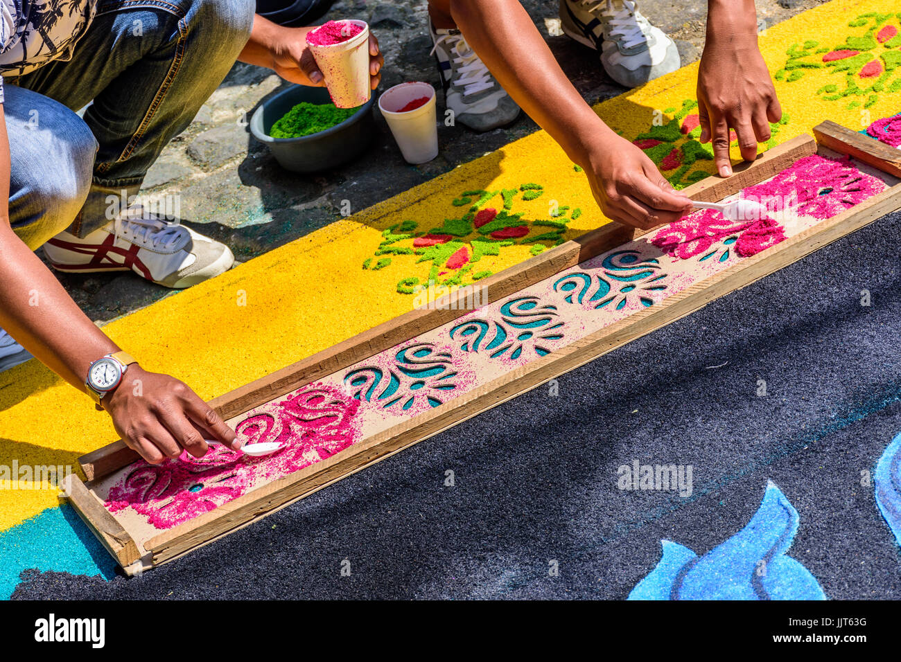 Antigua, Guatemala -  March 26, 2017: Locals spoon dyed sawdust through wooden stencil to decorate Lent carpet for procession Stock Photo