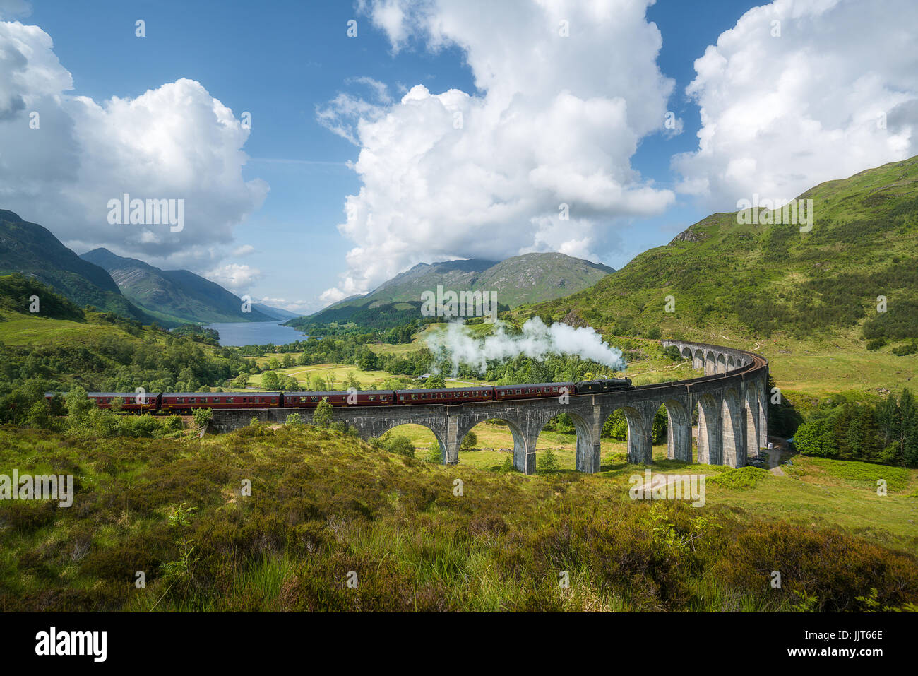 Vintage steam train passes the famous Glenfinnan viaduct with views over Loch Shiel Stock Photo