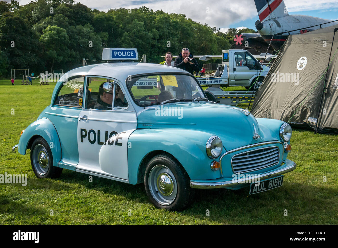 Man sitting in vintage Morris Minor police car, with couple taking a photo, Wheels and wings family day 2016, East Fortune, East Lothian, Scotland, UK Stock Photo