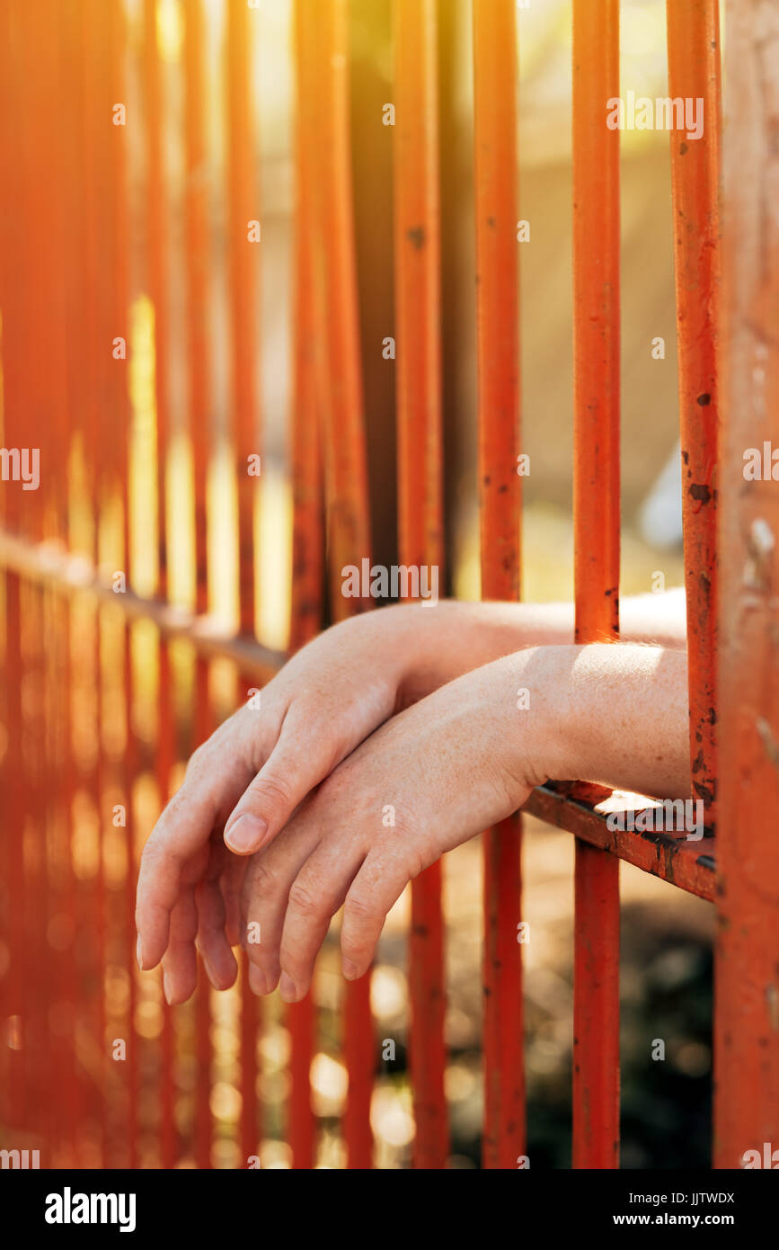 Female hands behind prison yard bars, incarcerated captivated person in jail Stock Photo
