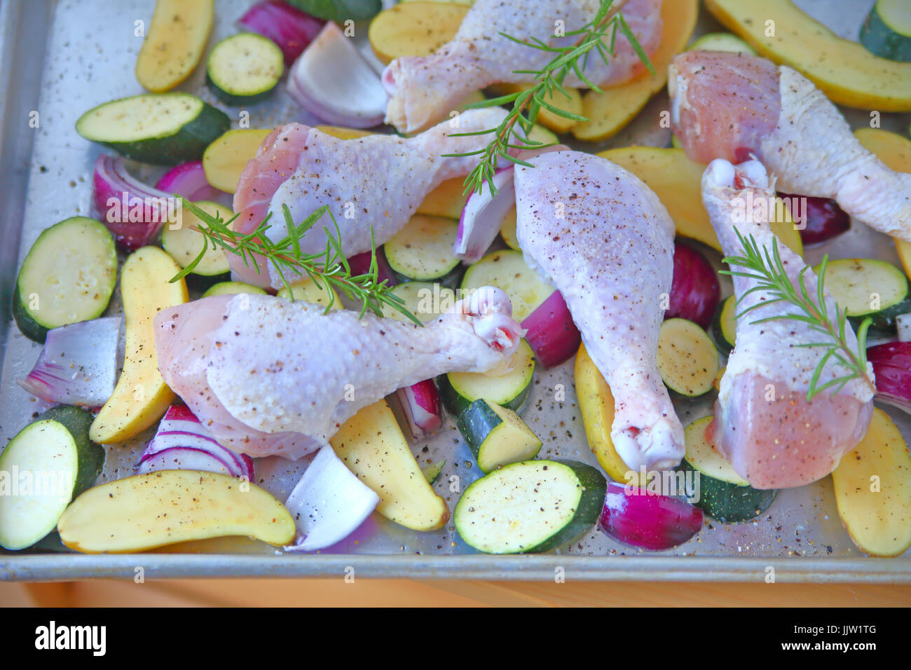 Baking pan with raw chicken legs, zucchini, red onion and fingerling potatoes, seasoned and ready to bake Stock Photo