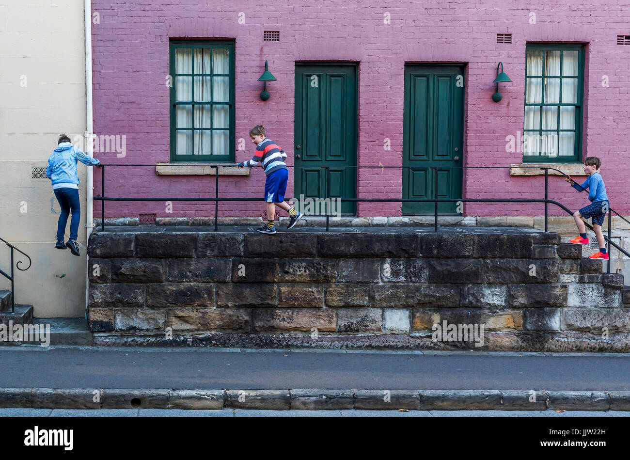 Three boys climbing on a staircase fence in front of a building at the Rocks in Sydney Australia Stock Photo