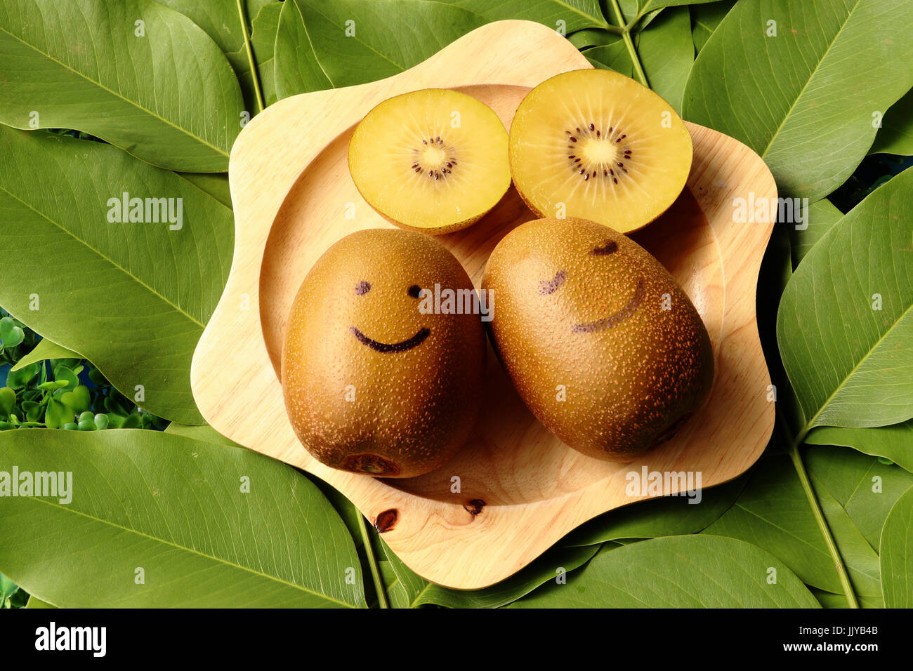 two happy kiwi fruit and pieceof sliced kiwi fruit in wooden tray on