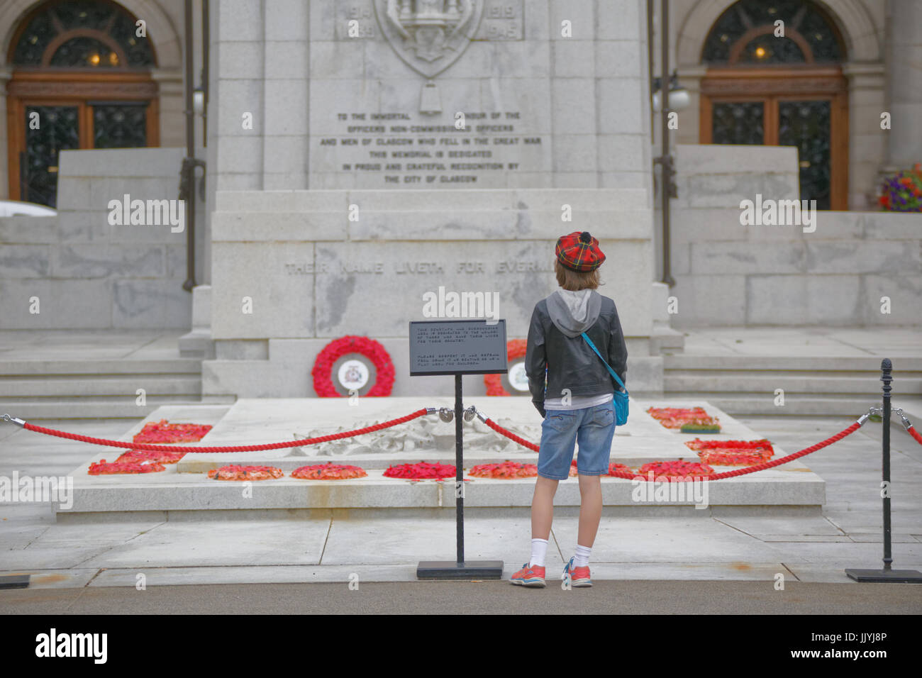 young teenage boy in tartan Tammy in front of the war memorial cenotaph George Square Glasgow red poppies Stock Photo