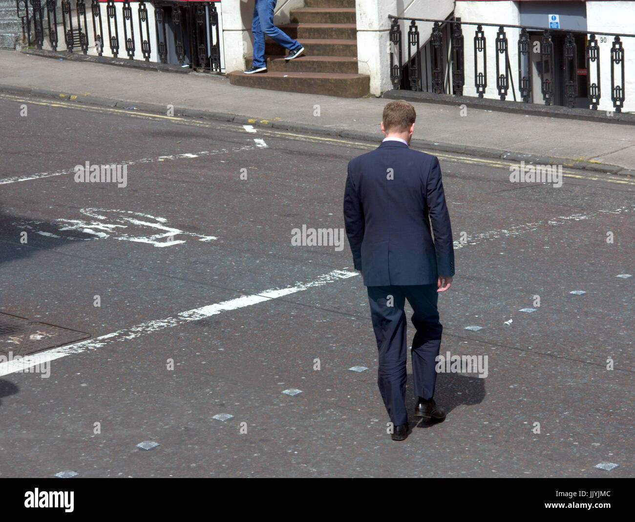 businessmen in suit crossing the street in Glasgow bike logo on road Stock Photo