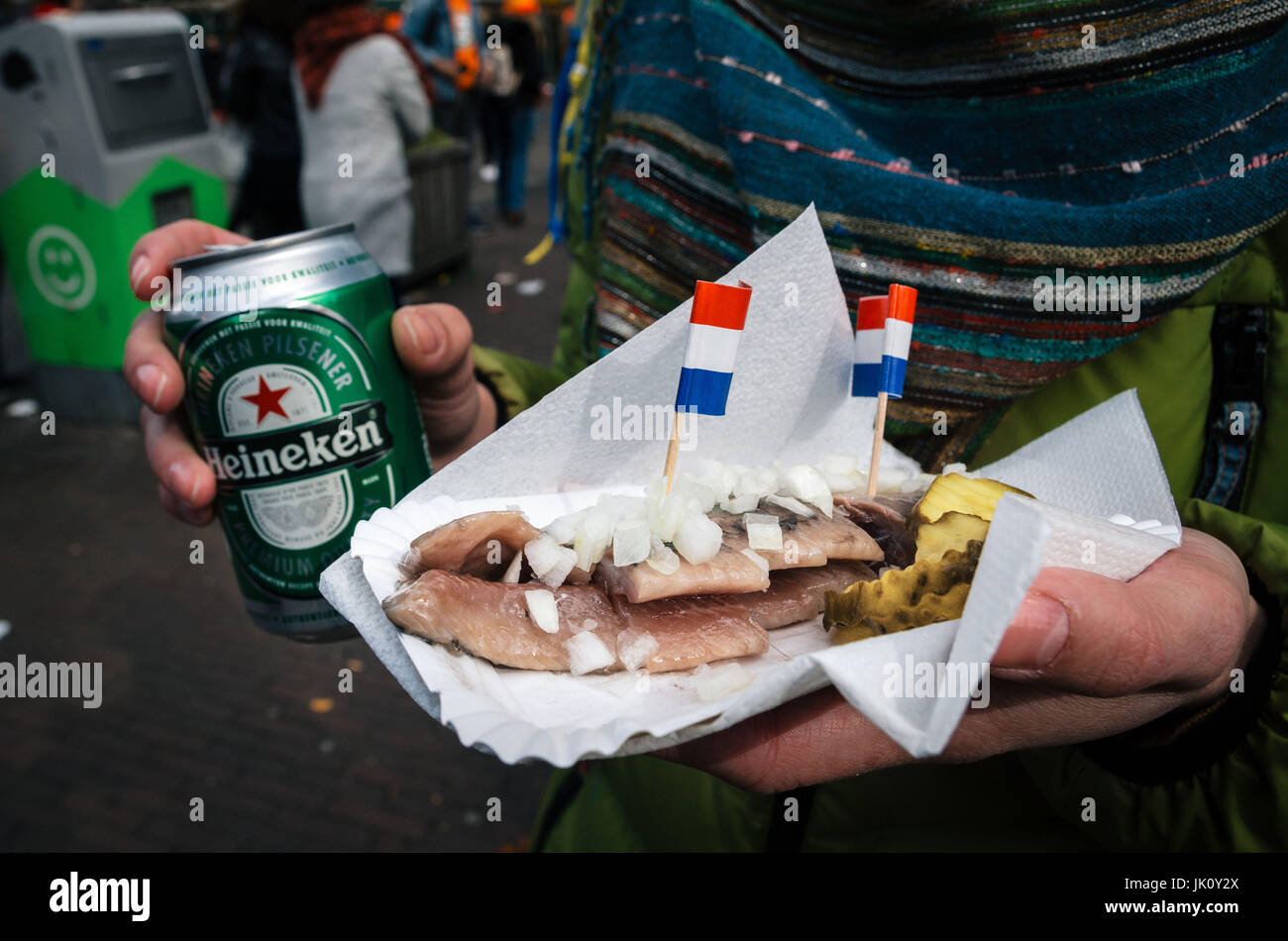 Amsterdam, Netherlands - 25 April, 2017: Hands hold a beer Heineken and a traditional Dutch delicacy of herring with gherkins and onions. Stock Photo