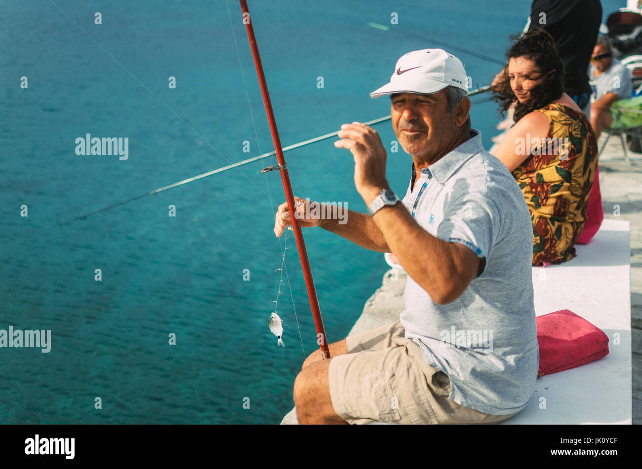 Pefkohori, Greece - May 26, 2015: Man wearing a cap shows his catch while fishing in the Aegean sea Stock Photo