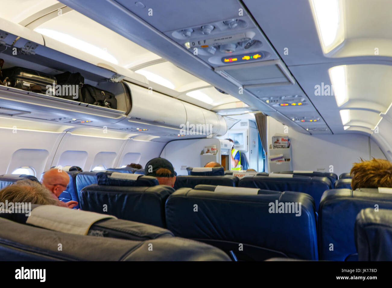 People seated on an aeroplane with open overhead luggage compartments Stock Photo