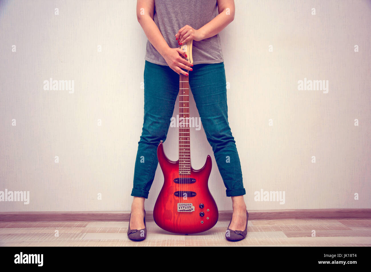 girl in high heels stands against the wall and holds the electric guitar. toned Stock Photo