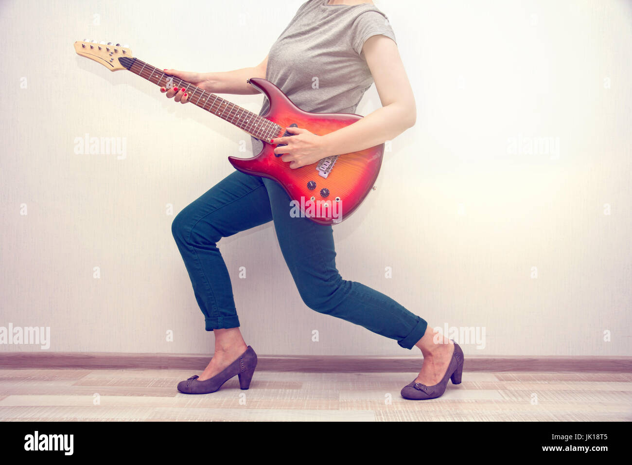 girl in a gray t-shirt and high heels dancing with electric guitar. toned Stock Photo