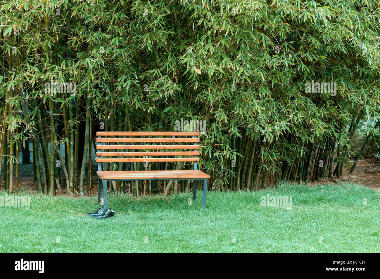 A wooden bench and black shoes against bamboo background. Stock Photo