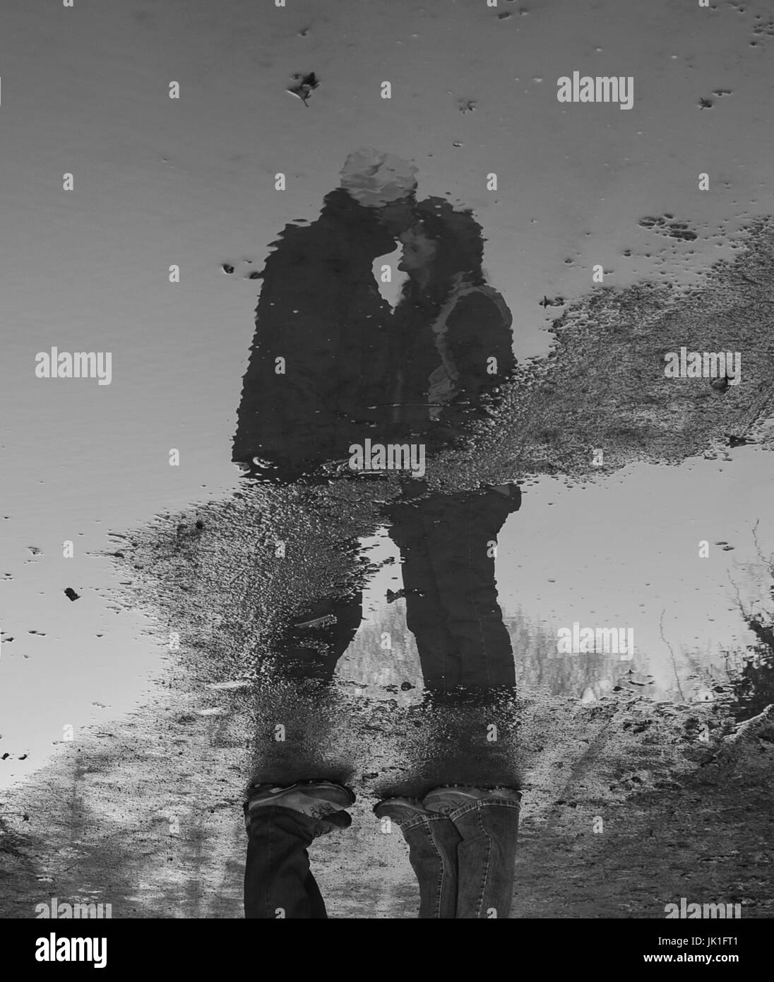 // Real Love. A couple's display of affection with a gentle kiss on the forehead reflected in a puddle. Stock Photo