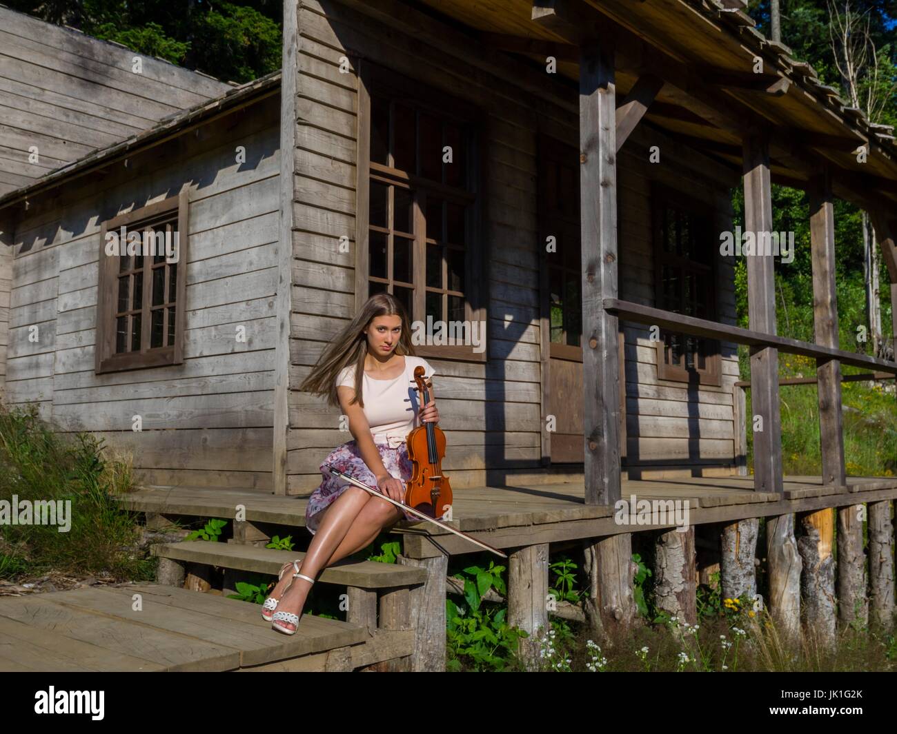 Countrygirl with violin sitting on porch wooden house looking at Stock