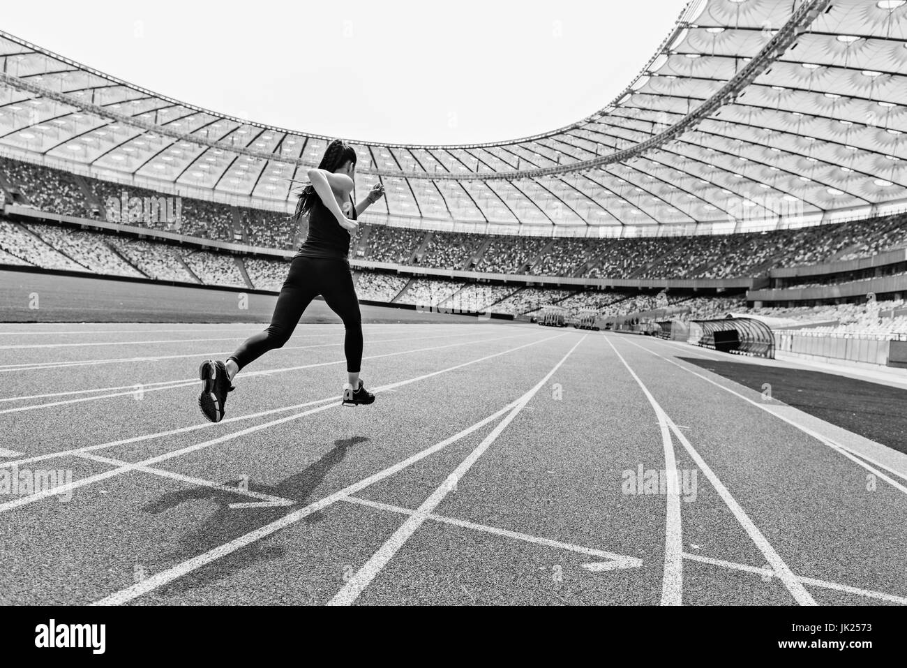 Back view of young fitness woman in sportswear sprinting on running track stadium, black and white photo Stock Photo