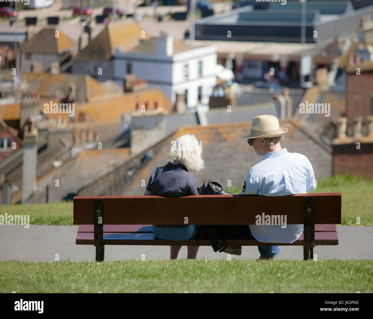 Senior couple sitting on a park bench overlooking a town. Stock Photo
