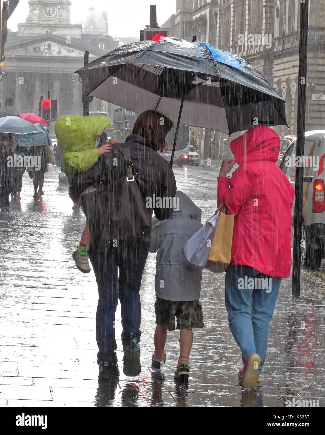 torrential rain lashing pouring down in Glasgow umbrella and hoods family carrying child Stock Photo