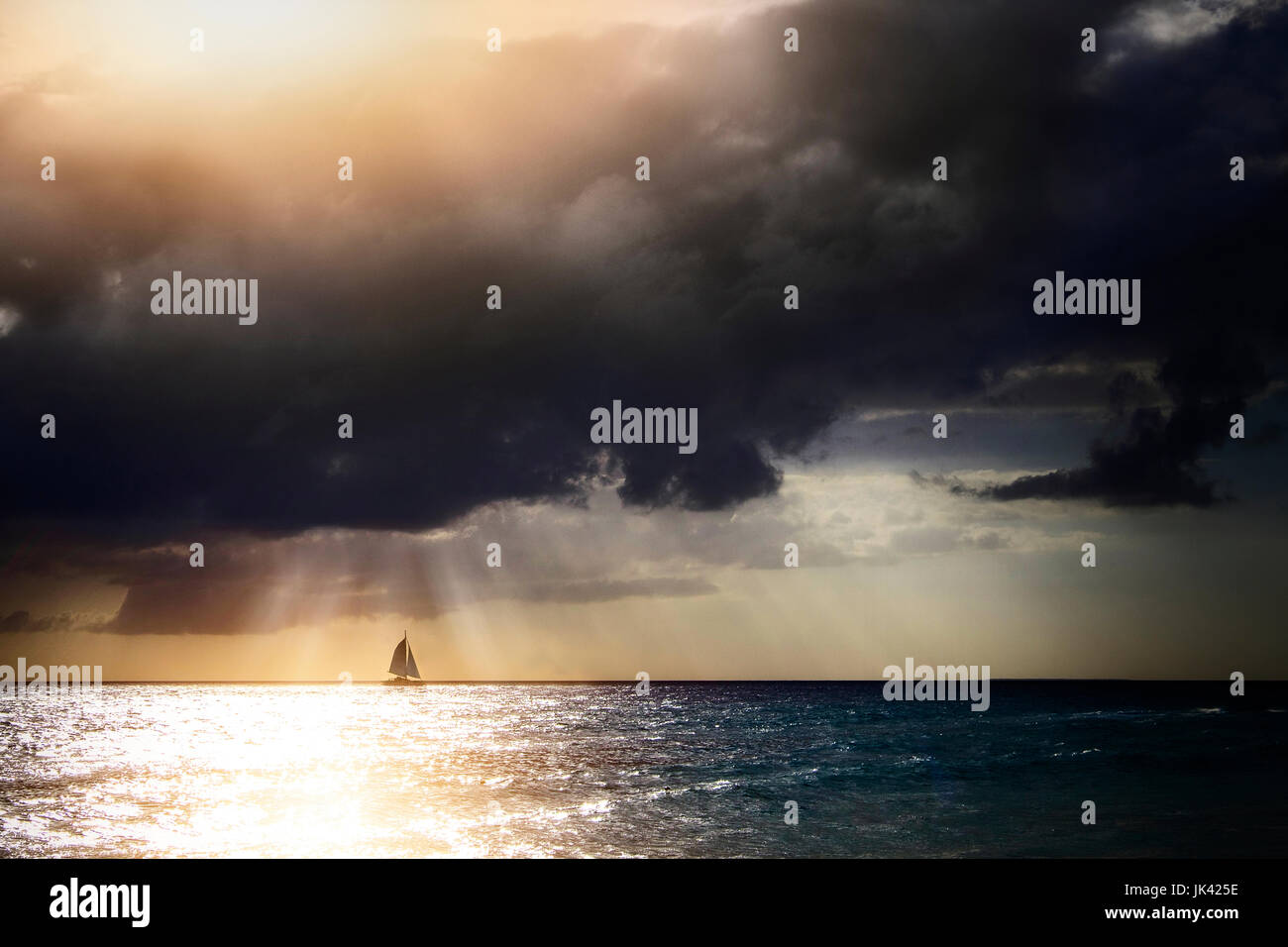 Sunbeams through storm clouds over sailboat Stock Photo