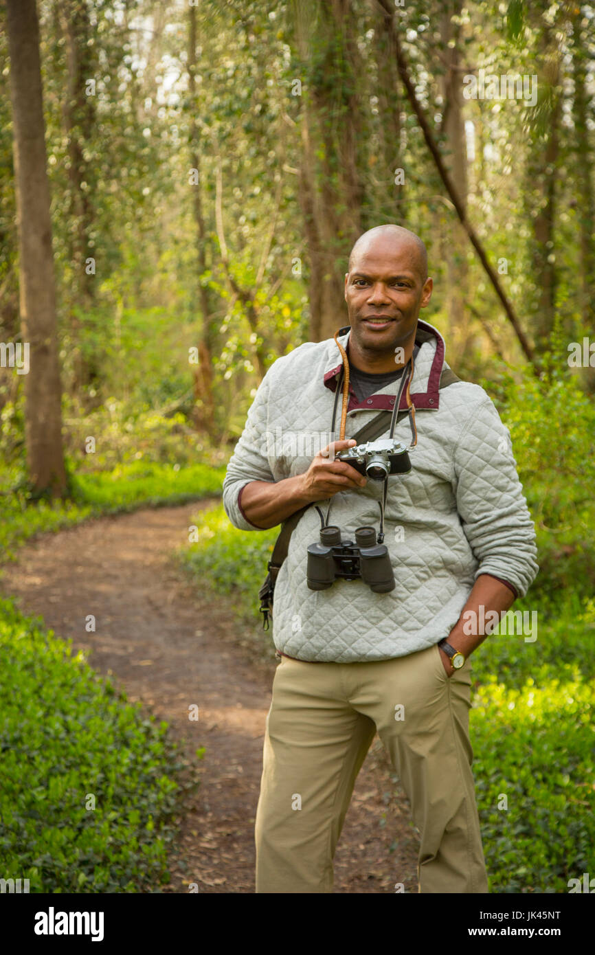 African American man standing on path in forest holding camera Stock Photo