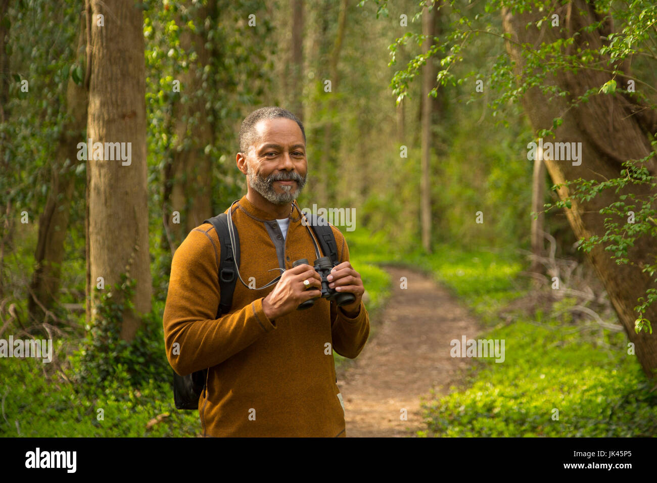 African American man standing on path in forest holding binoculars Stock Photo