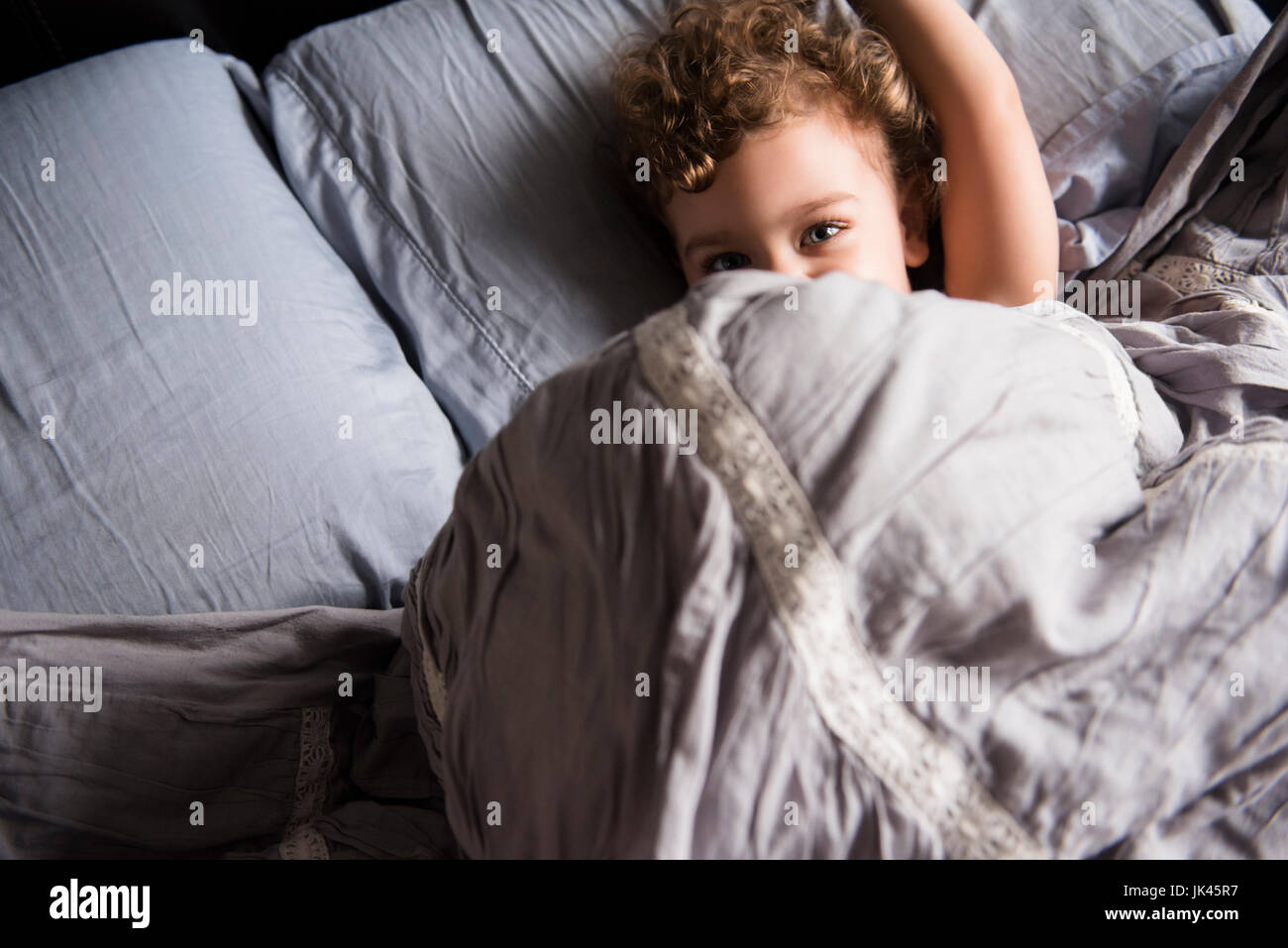 Caucasian boy hiding under blanket in bed Stock Photo