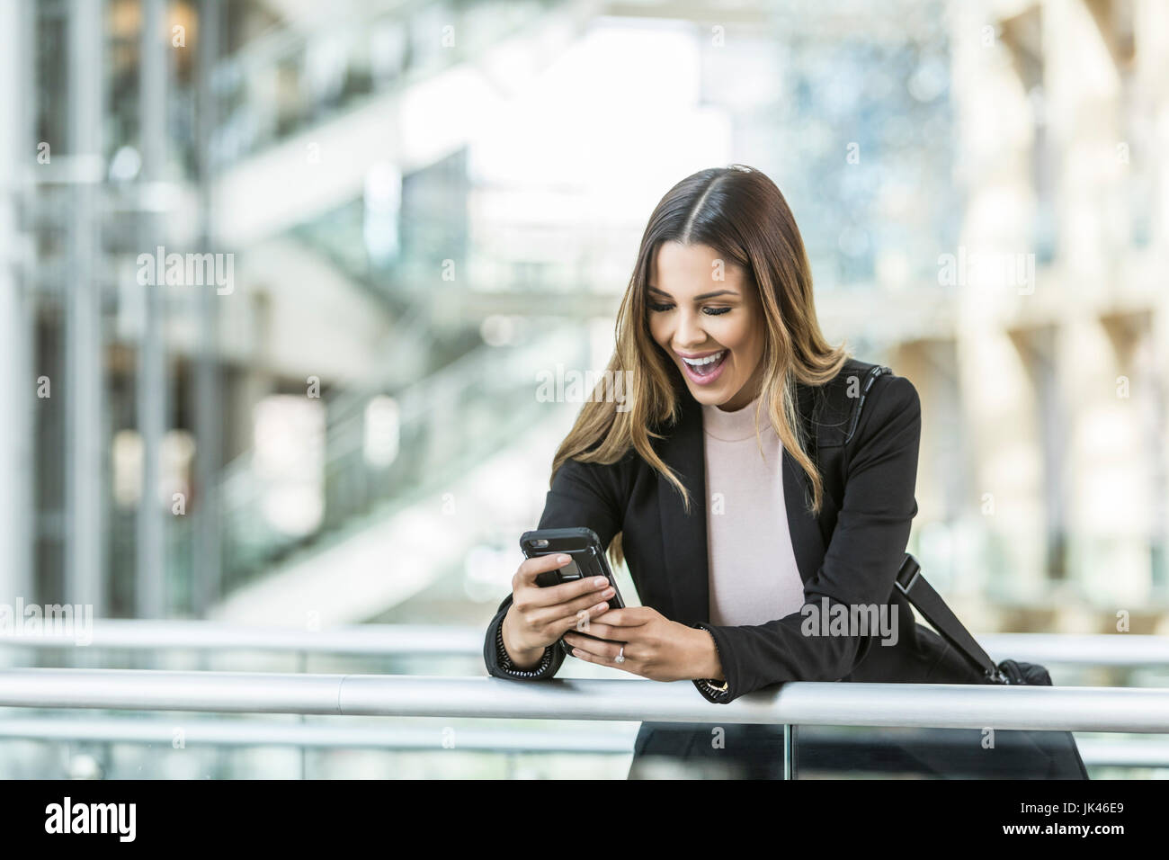 Mixed Race businesswoman texting on cell phone leaning on railing in lobby Stock Photo