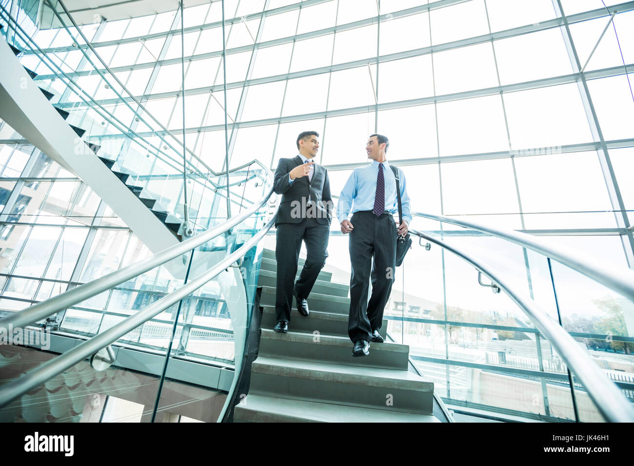 Smiling Mixed Race businessmen descending staircase and talking Stock Photo