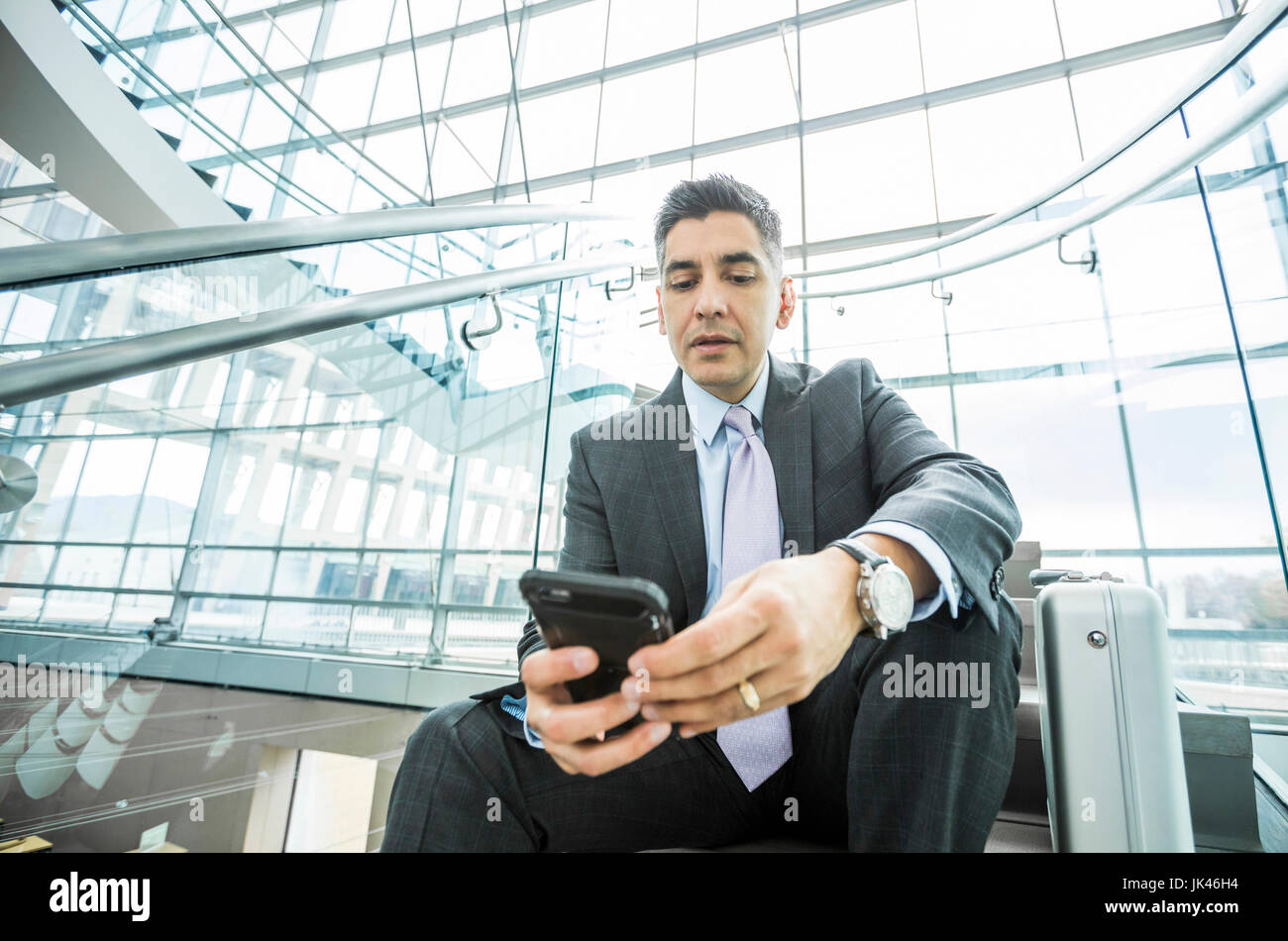 Serious Mixed Race businessman sitting on staircase texting on cell phone Stock Photo