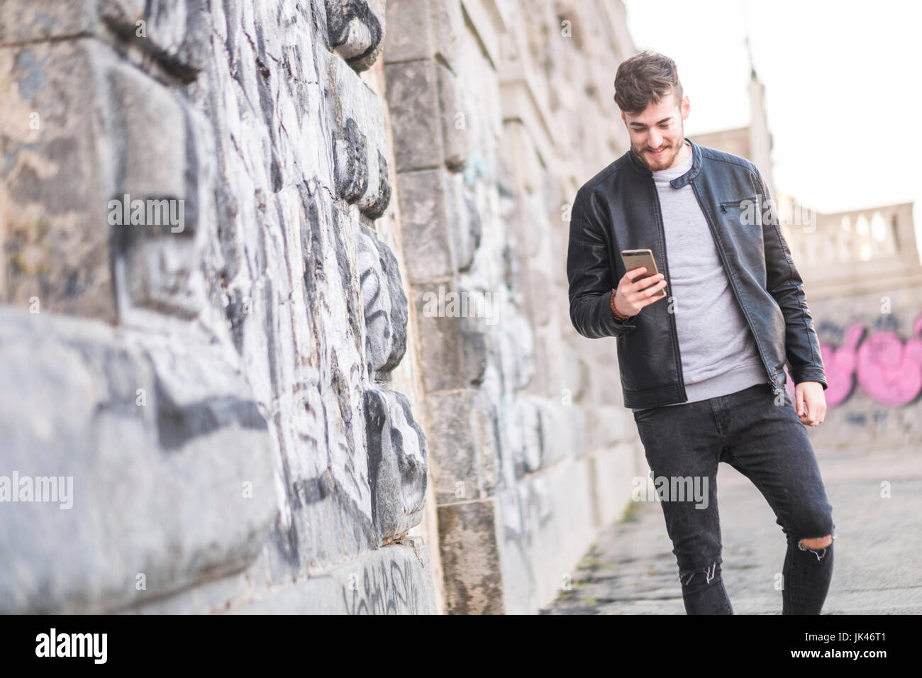Smiling Caucasian man walking on sidewalk texting on cell phone Stock Photo