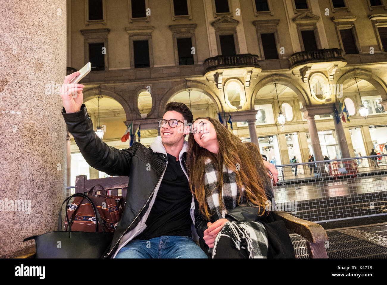 Caucasian couple sitting on urban bench posing for cell phone selfie Stock Photo