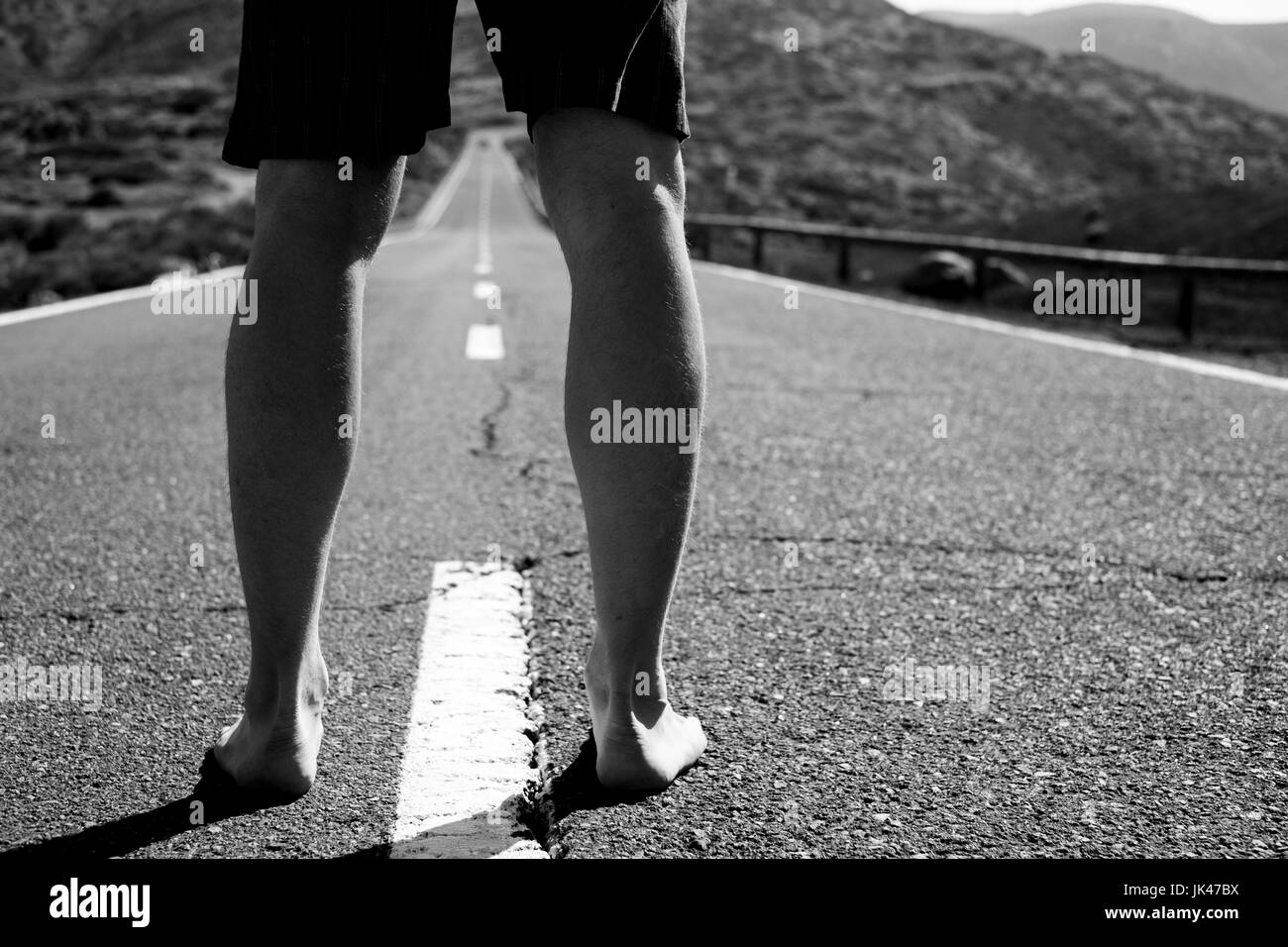 Legs of barefoot Caucasian man standing in middle of road Stock Photo