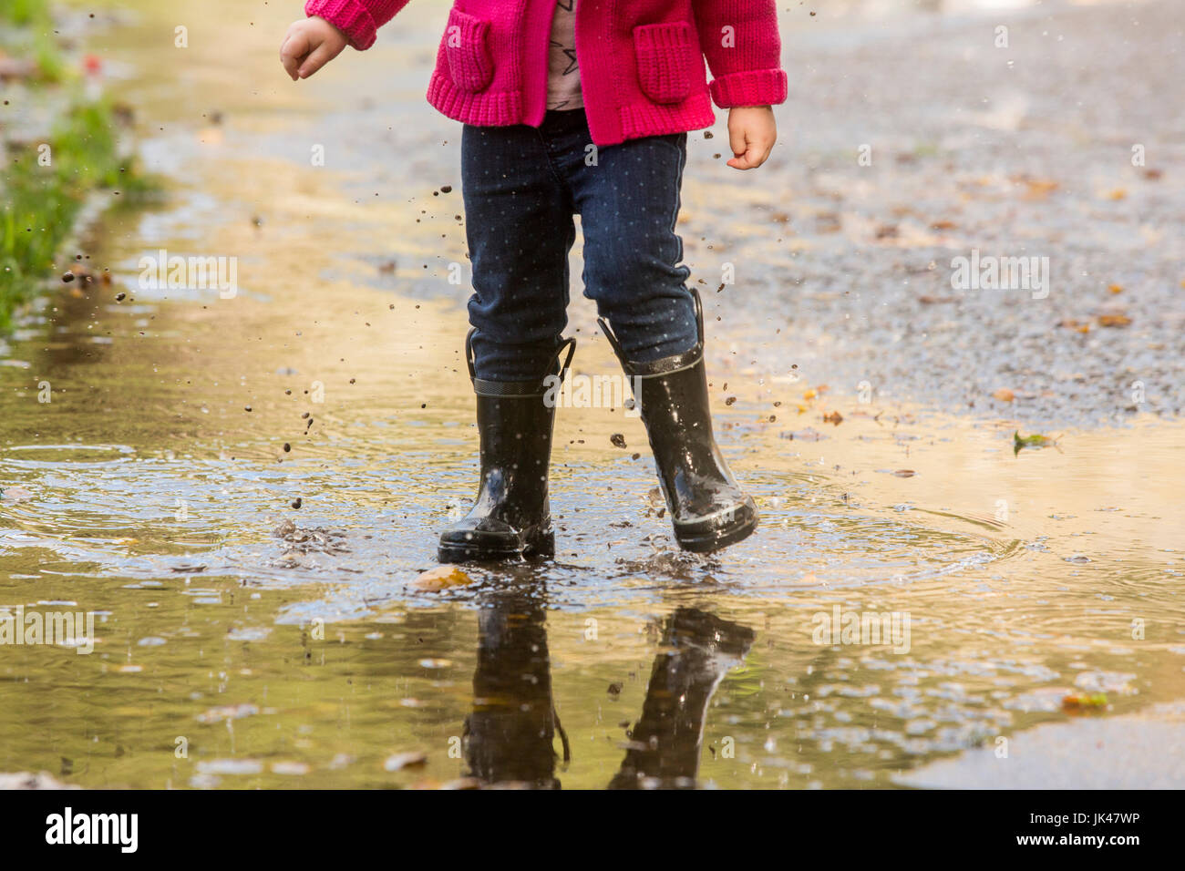 Caucasian girl wearing boots splashing in puddle Stock Photo