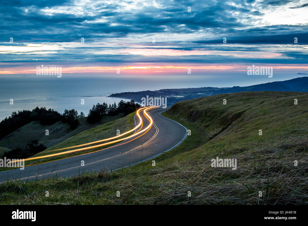 Light trails on winding road near ocean Stock Photo