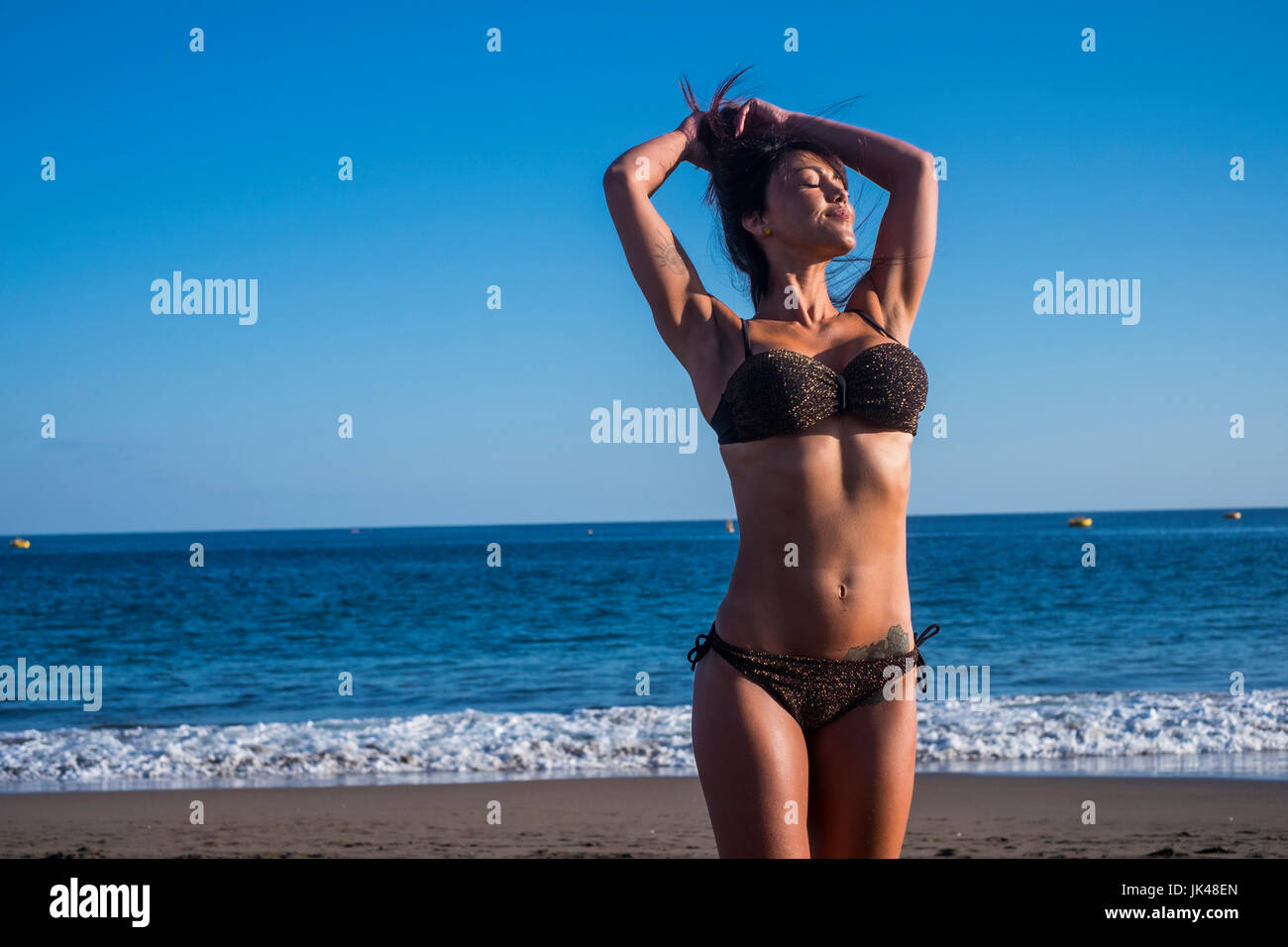 Caucasian woman standing on beach with hands in hair Stock Photo