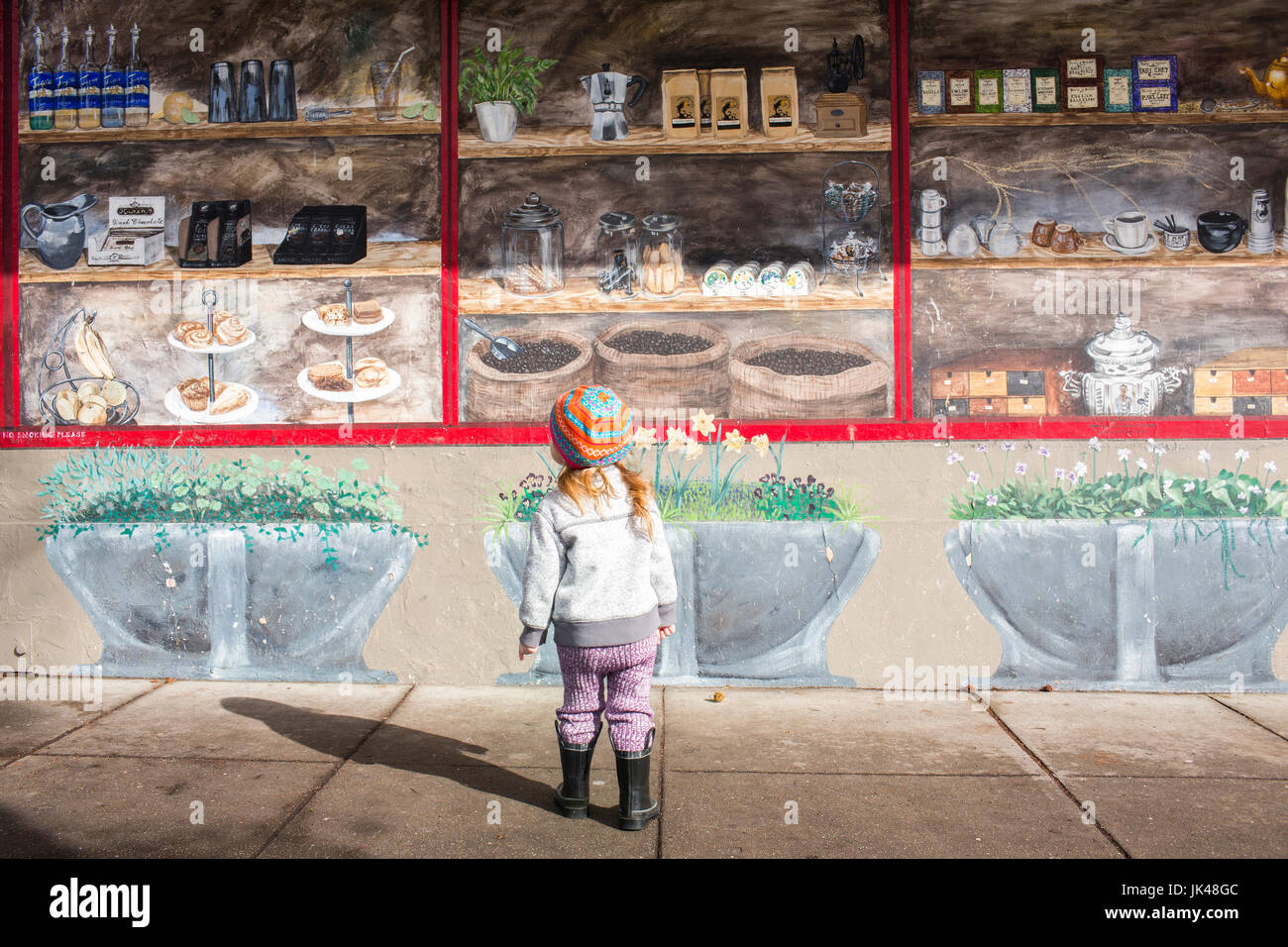 Caucasian girl standing on sidewalk admiring mural on wall Stock Photo