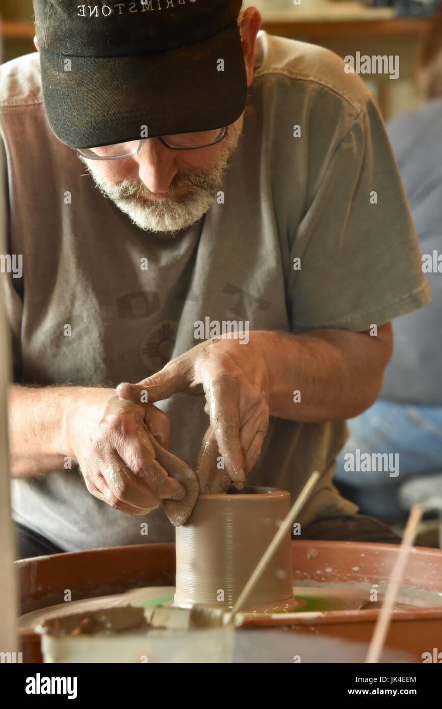 Middle aged man forming clay for a cup on a spinning wheel at Yourist