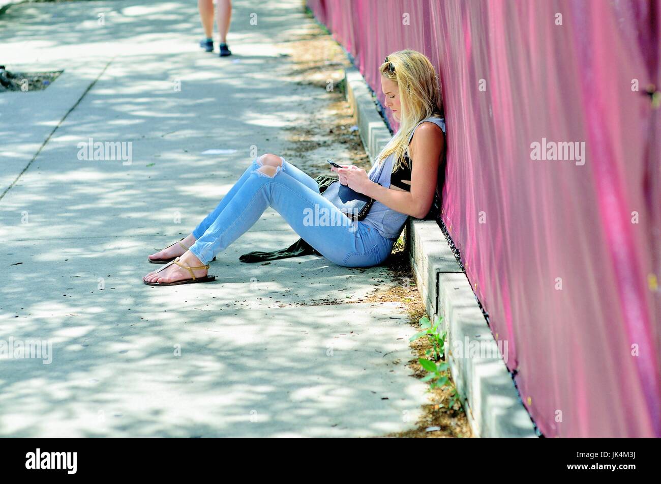 Chicago, Illinois, USA. Young woman seated on a sidewalk while checking her phone near DePaul University in Chicago. Stock Photo