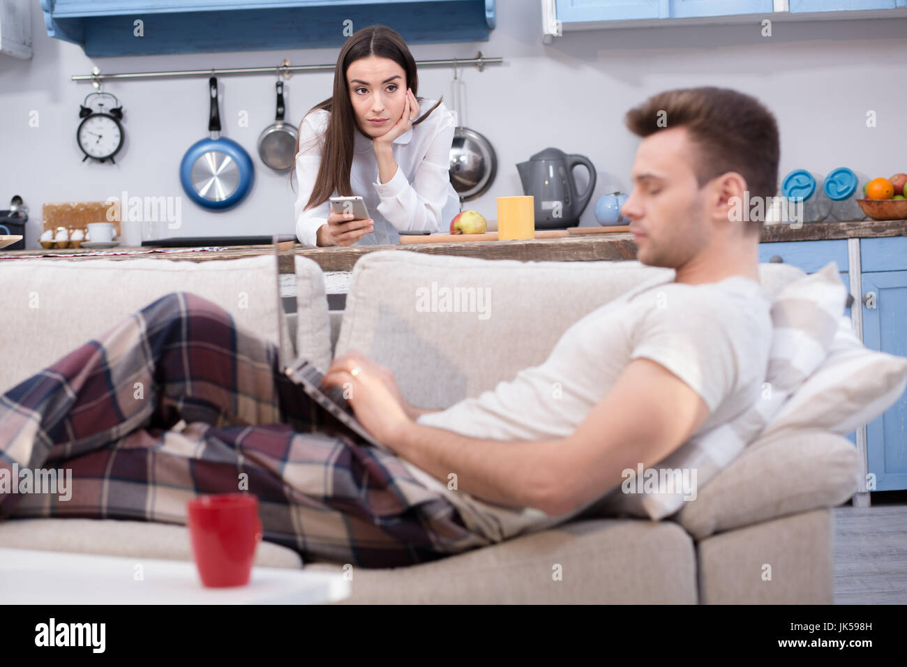 Working woman looking seriously on her lazy husband. Stock Photo