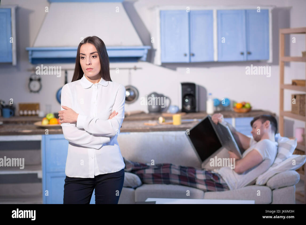 Woman in business clothes staning offended by her lazy husband. Stock Photo