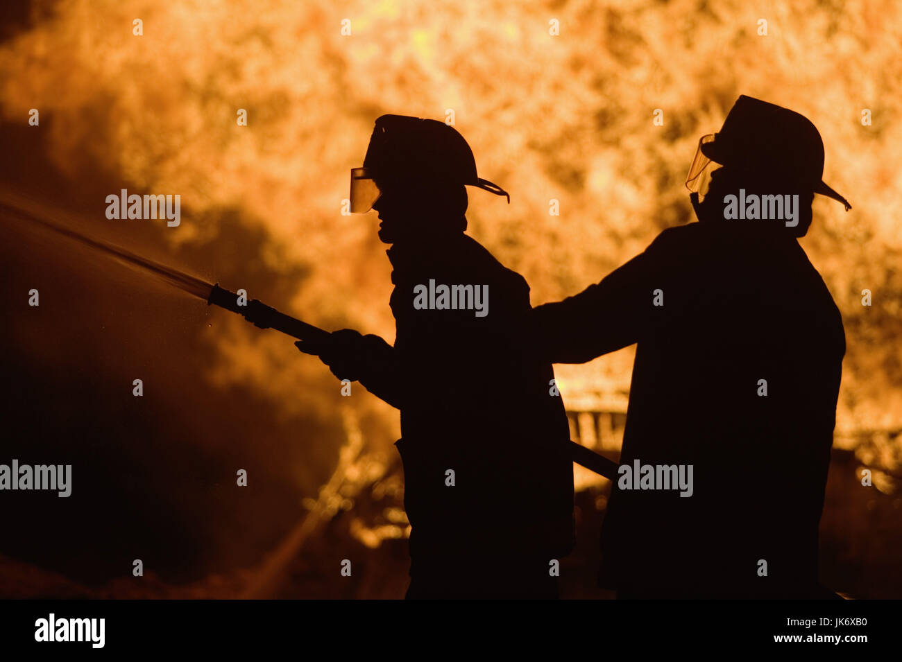 Silhouette, Feuerwehrmänner,  Brandbekämpfung, Detail, seitlich  Berufsfeuerwehr, Männer, Schutzkleidung, Beruf, Berufsfeuerwehr, Berufsfeuerwehrmänner, Feuer, Flammen, brennen, löschen, Löscharbeiten, Feuerwehreinsatz, Hilfeleistung, Wasserschlauch, Feuerwehrschlauch, Wasser, Katastrophe, Brandkatastrophe, brennen, lodern, Hitze, Zerstörung, Gefahr, verbrennen, Vernichtung, gefährlich, Gefahrensituation, 'lichterloh brennen', Hausbrand, Gebäudebrand, Symbol, Konzept, brandheiß, lodern, knistern, Rettung, Bekämpfung, Feuerwehrleute Stock Photo