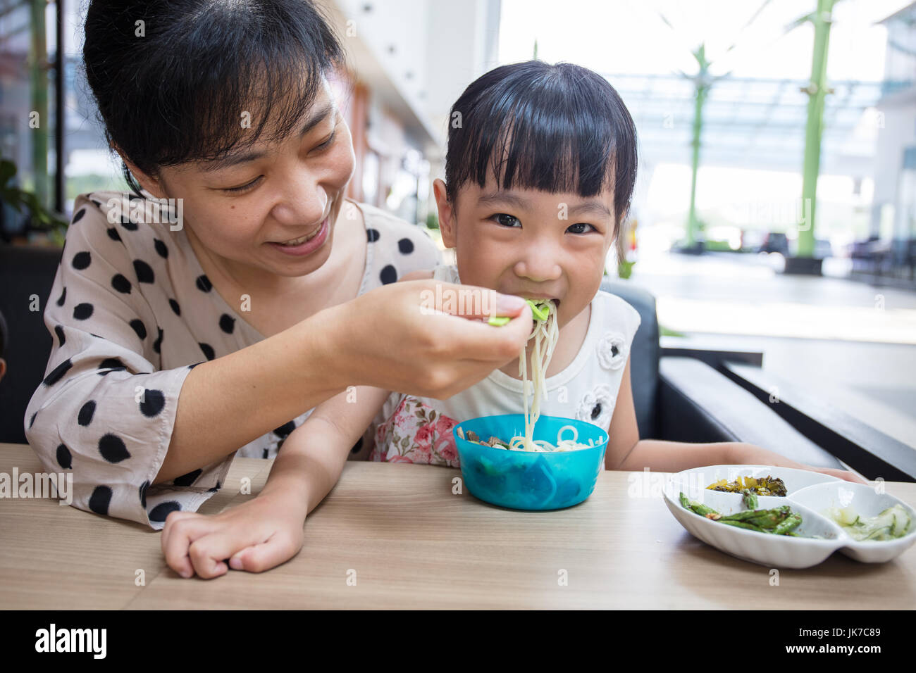 Asian Chinese mother and daughter eating beef noodles in outdoor cafe Stock Photo