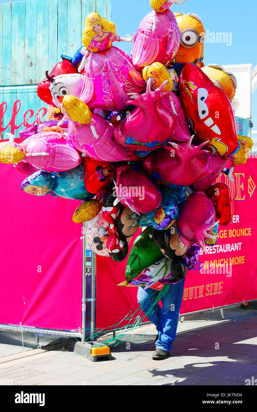 Man holding and hidden by a large bunch of helium balloons on Pier head