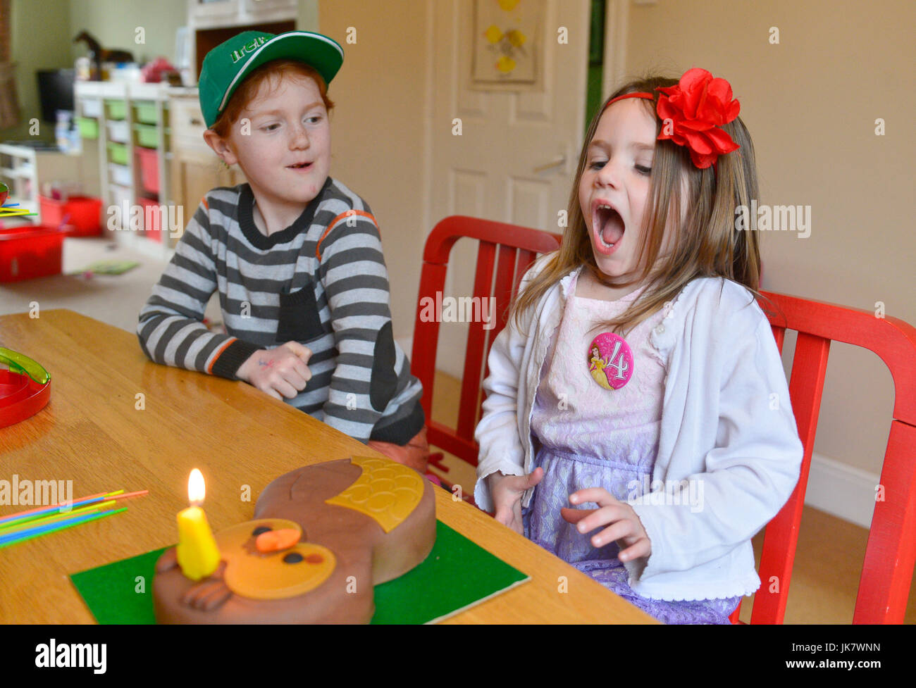 sister looks on as four year old sister blows out birthday cake candle