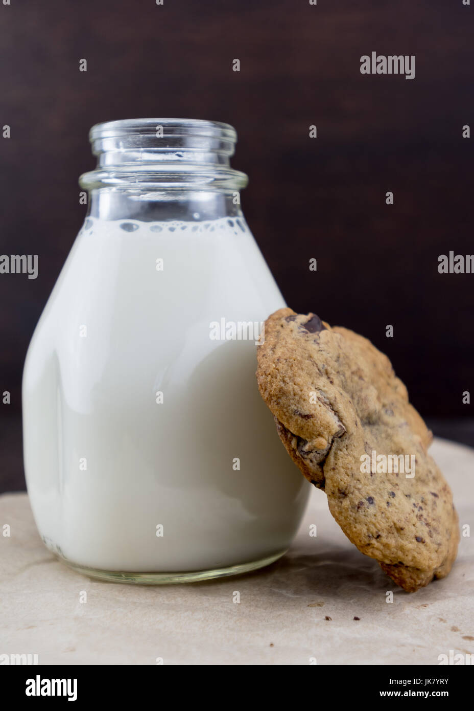 Single Chocolate Chip Cookie Leaning Against Jar of Milk in Vintage Bottle Stock Photo